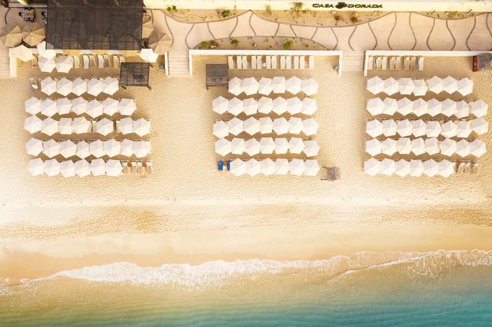 Aerial view of beach resort with organized white umbrellas, sand, and turquoise ocean water
