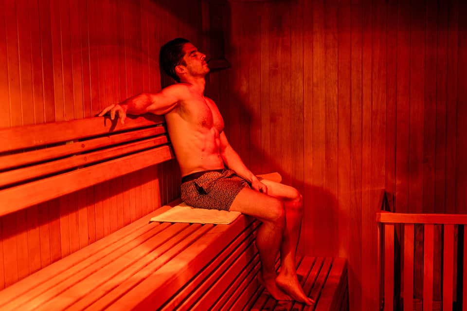 Man relaxing in a sauna with red-orange heated benches and wooden walls