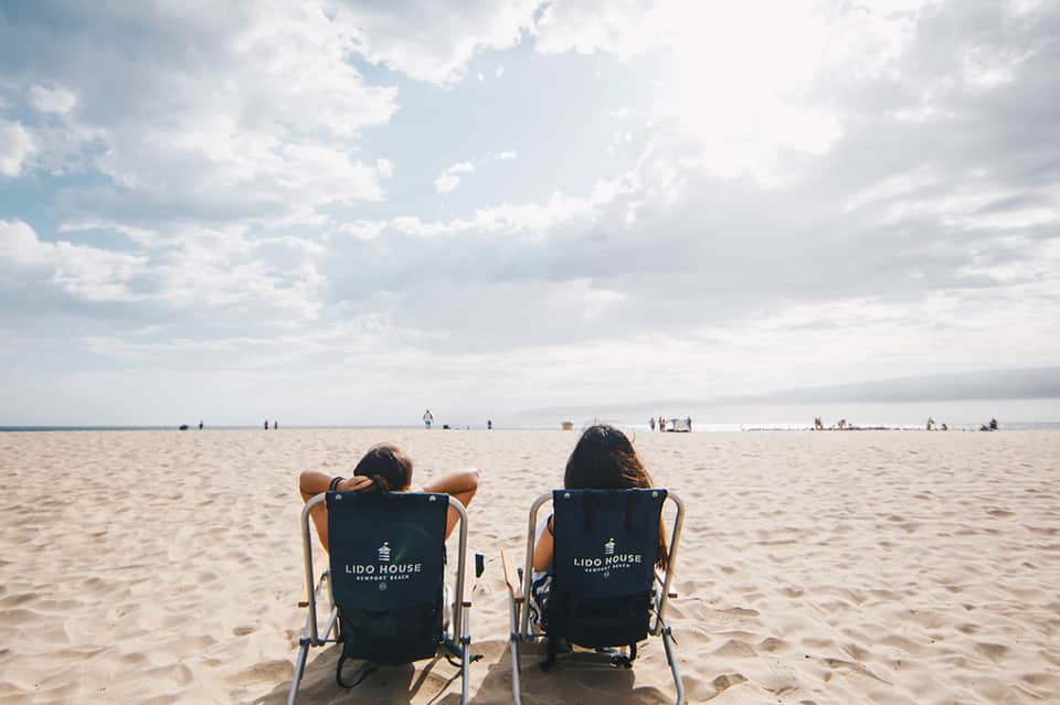 Two women relaxing in beach chairs on sandy shore facing calm ocean water