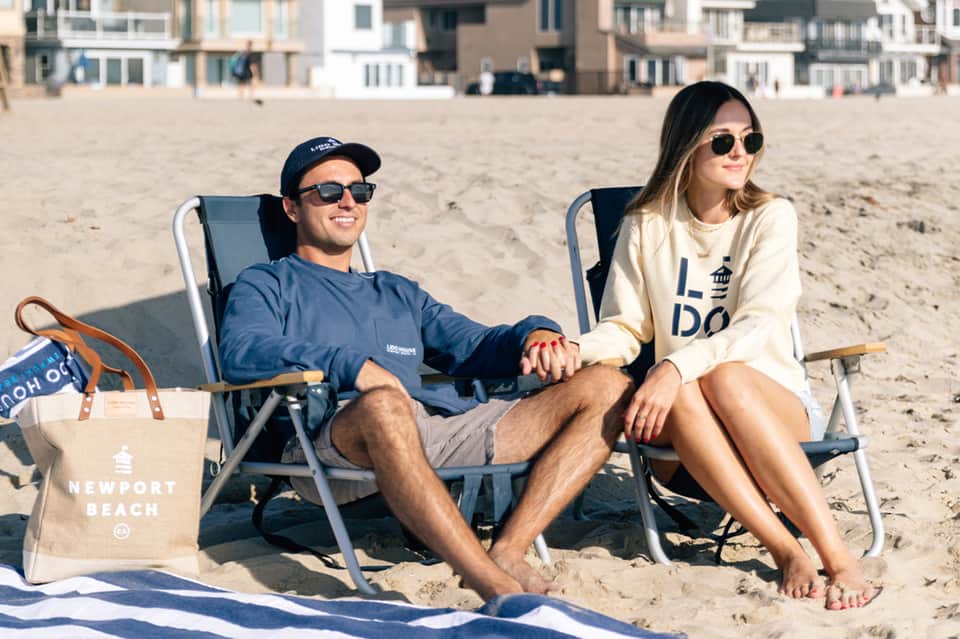 Couple relaxing on beach chairs with ocean view and residential buildings in background
