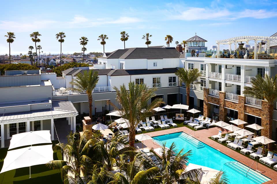 Aerial view of resort pool surrounded by white lounge chairs and tropical palm trees