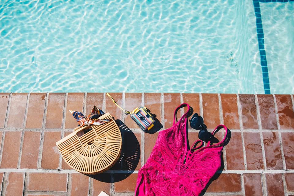 Overhead view of turquoise pool with terracotta deck, beach bag, and swimwear