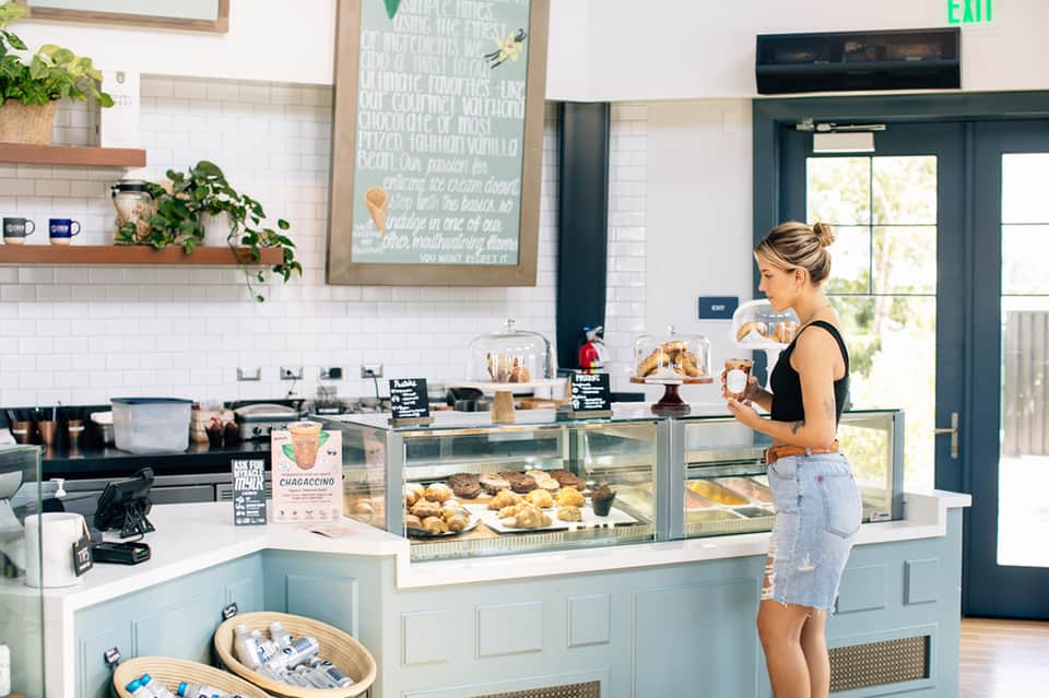 Casual café interior with white subway tile, wooden shelves, bakery display case, and green door