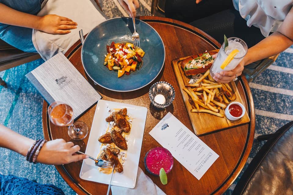 Overhead view of casual dining with plated dishes, fries, cocktails, and menu on wooden table