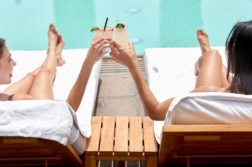 Guests relaxing poolside with tropical cocktails and blue water backdrop