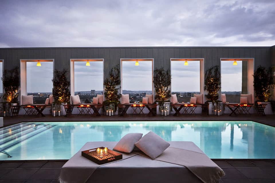 Rooftop pool at night with city skyline view, lounge seating, and ambient lighting