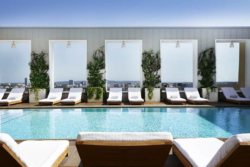 Rooftop pool with city skyline view, white lounge chairs, large white privacy screens, and landscaping