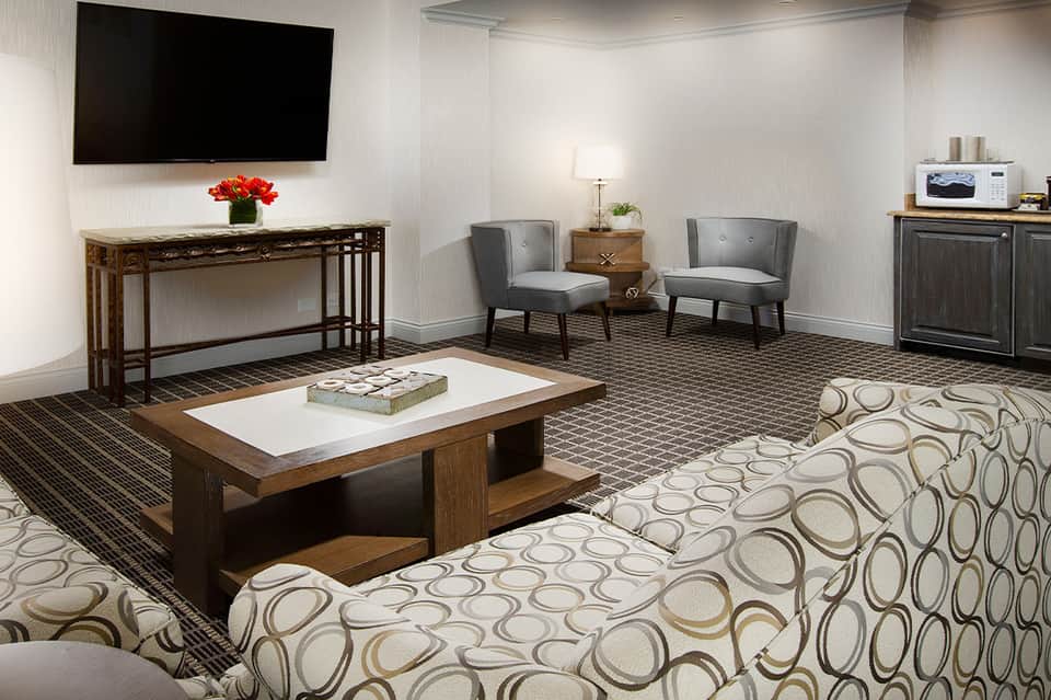 Contemporary hotel lounge with wooden furniture, patterned carpet, TV, and neutral decor