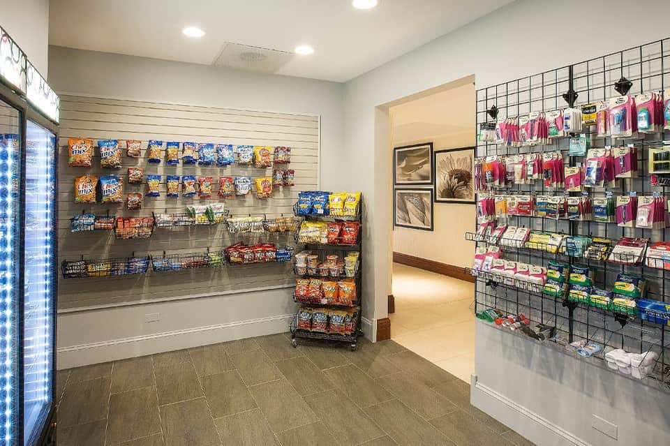 Hotel convenience store with slat wall displaying packaged snacks, refrigerated beverages, and merchandise with bright lighting
