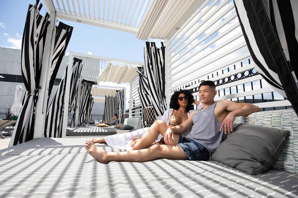 Couple relaxing on cushioned seating under striped pergola canopy