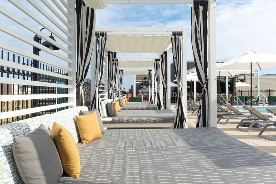 Covered cabana lounge with striped curtains, yellow and gray cushions, and rooftop pool deck with lounge chairs