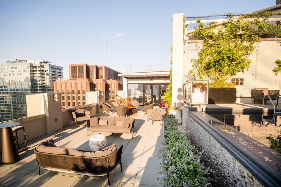 Urban rooftop terrace with modern furnishings, architectural building backdrop, and greenery