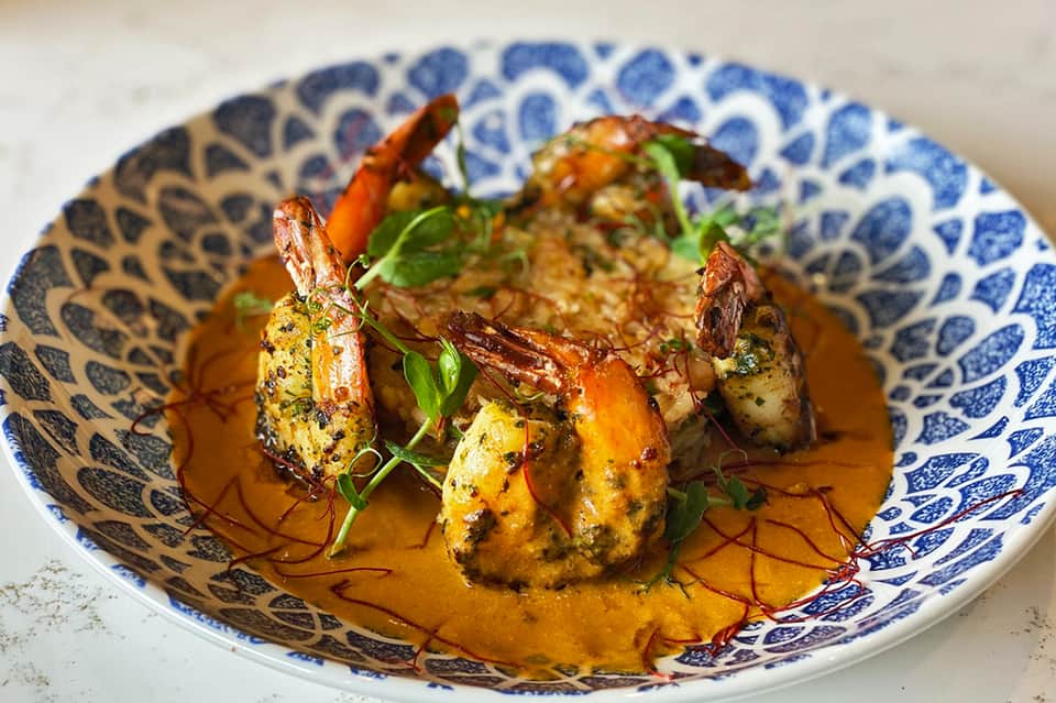 Grilled shrimp appetizer on blue and white patterned plate with sauce and green garnish