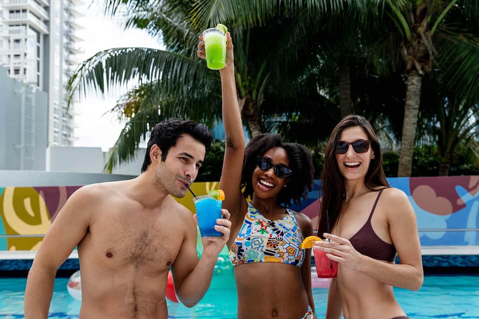 Three people in swimwear enjoying cocktails by a colorful resort pool