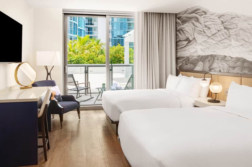 Modern hotel room with two queen beds, balcony access, and contemporary furnishings