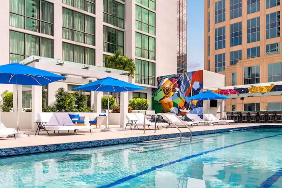 Resort pool with blue umbrellas, loungers, colorful mural art, and modern building backdrop