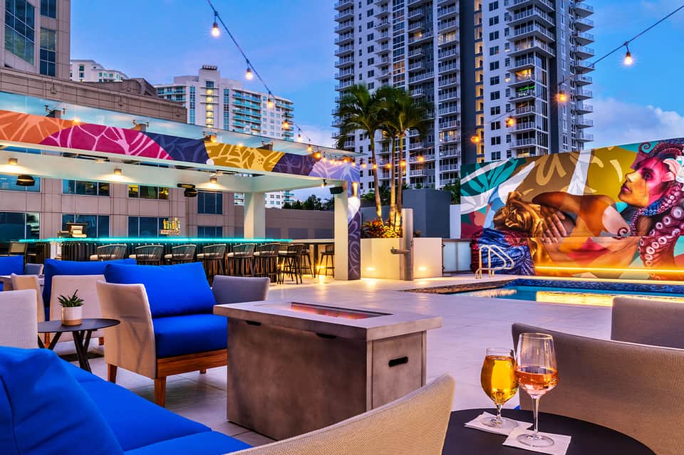 Rooftop pool deck with colorful mural art, blue lounge furniture, and evening city lights