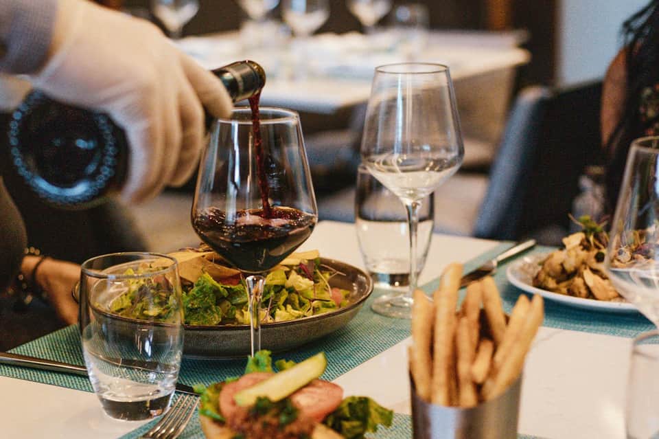 Wine being poured into glass at fine dining table with salad, water glass, and place settings