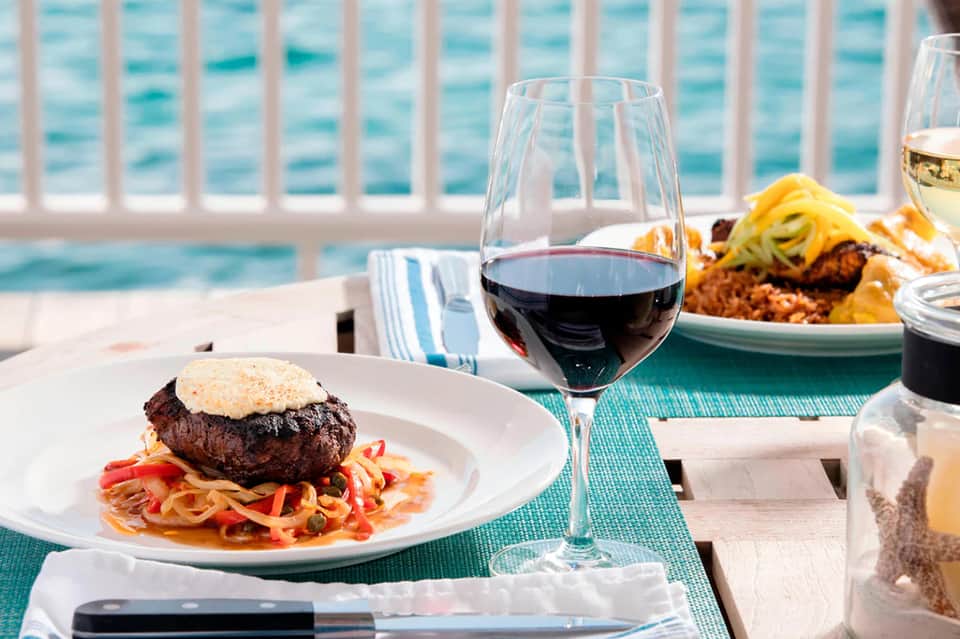 Fine dining beachfront table with steak burger, wine glass, and ocean view through railing