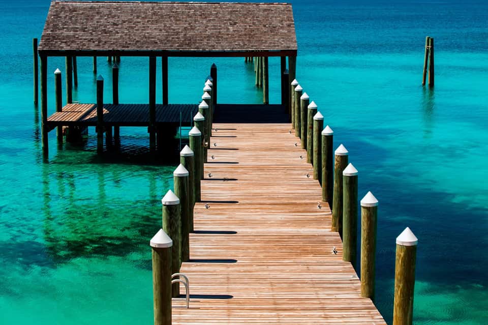 Wooden dock extending into crystal clear turquoise water with thatched-roof cabana and wooden pilings