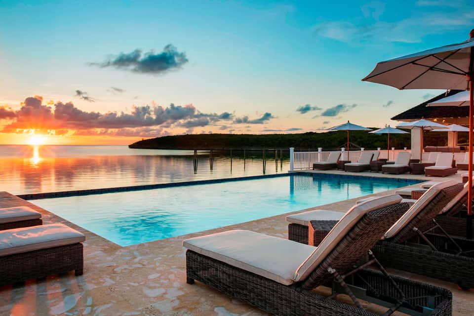 Infinity pool at sunset with lounge chairs, umbrellas, ocean view, and dramatic sky