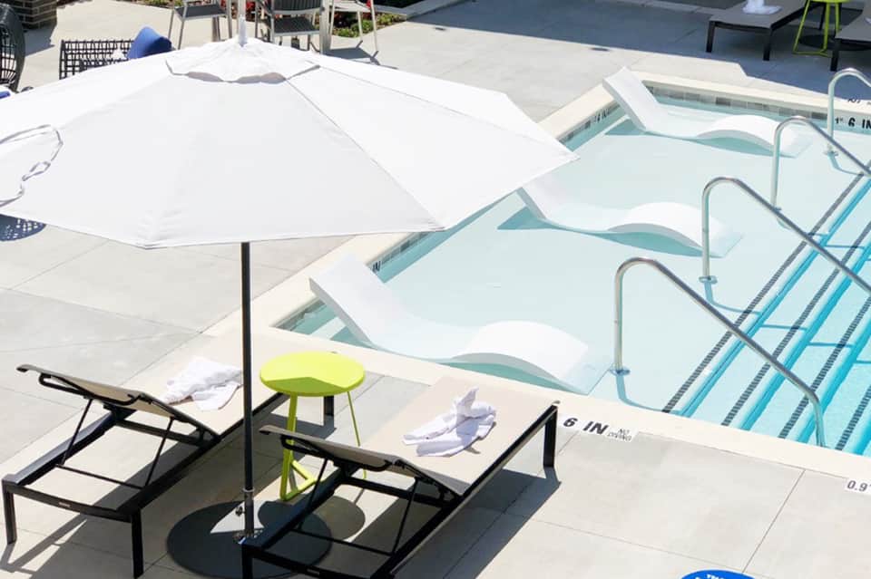 Resort pool deck with white umbrella, lounge chairs, and spa pools