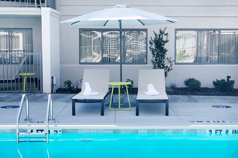Modern poolside lounge with white loungers, umbrella, and spa building