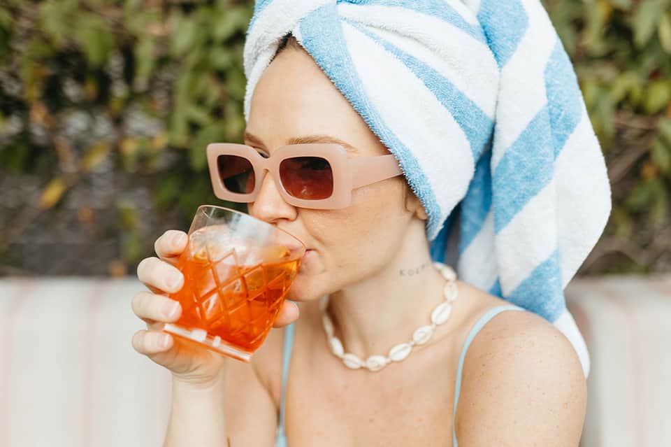 Woman in sunglasses and towel wrap enjoying tropical beverage by poolside