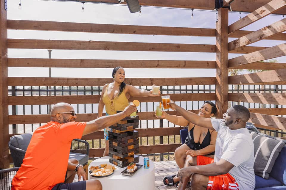 Group of friends playing games and socializing on beachfront deck with ocean backdrop