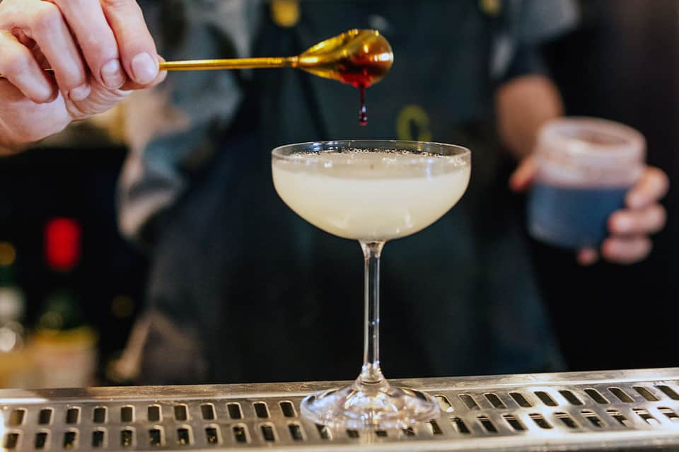 Bartender preparing cocktail with gold bar spoon over coupe glass