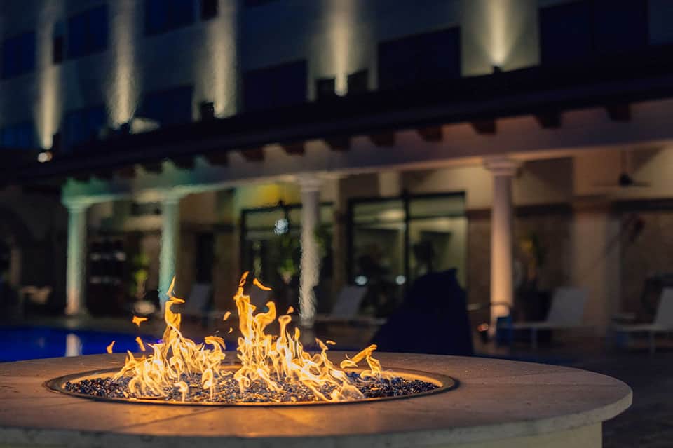 Fire pit glowing at night with illuminated hotel building and pool in background
