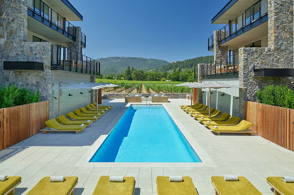 Resort infinity pool with yellow loungers flanked by stone buildings and mountain forest views