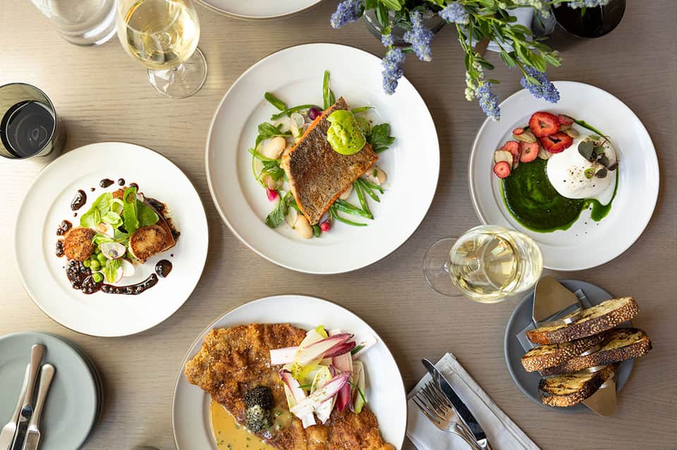 Overhead view of fine dining plates with seafood and vegetables, white wine, and floral centerpiece