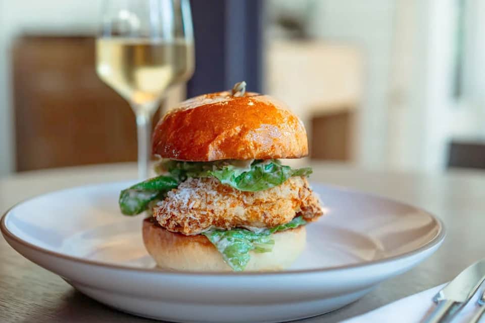 Gourmet burger with greens on white plate paired with white wine