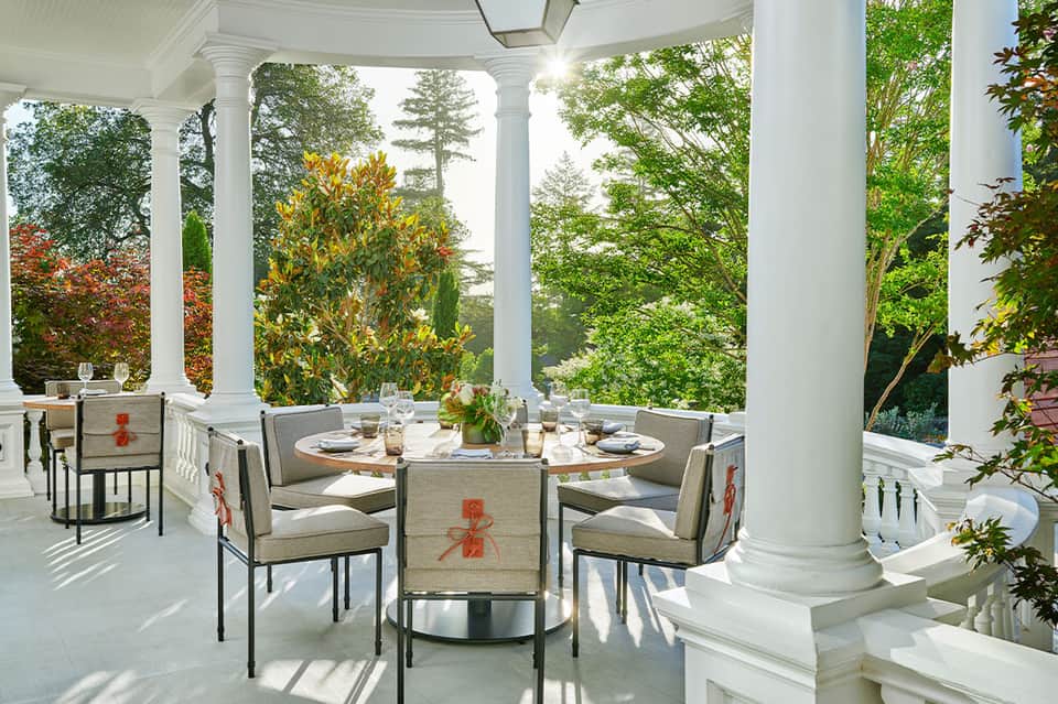 Outdoor covered porch with white columns, dining table, and garden views