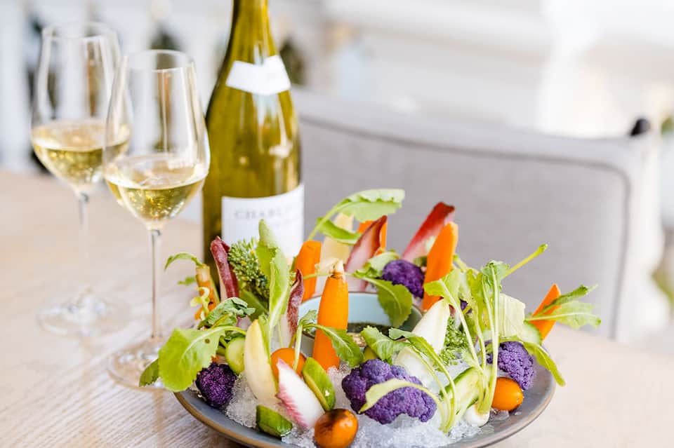 Fine dining presentation with white wine, champagne bottle, and colorful vegetable appetizer arrangement