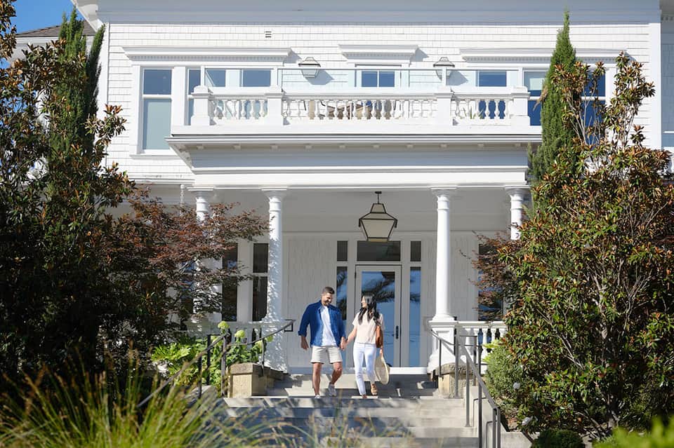 Couple walking toward modern white beachfront building with columns and manicured landscaping