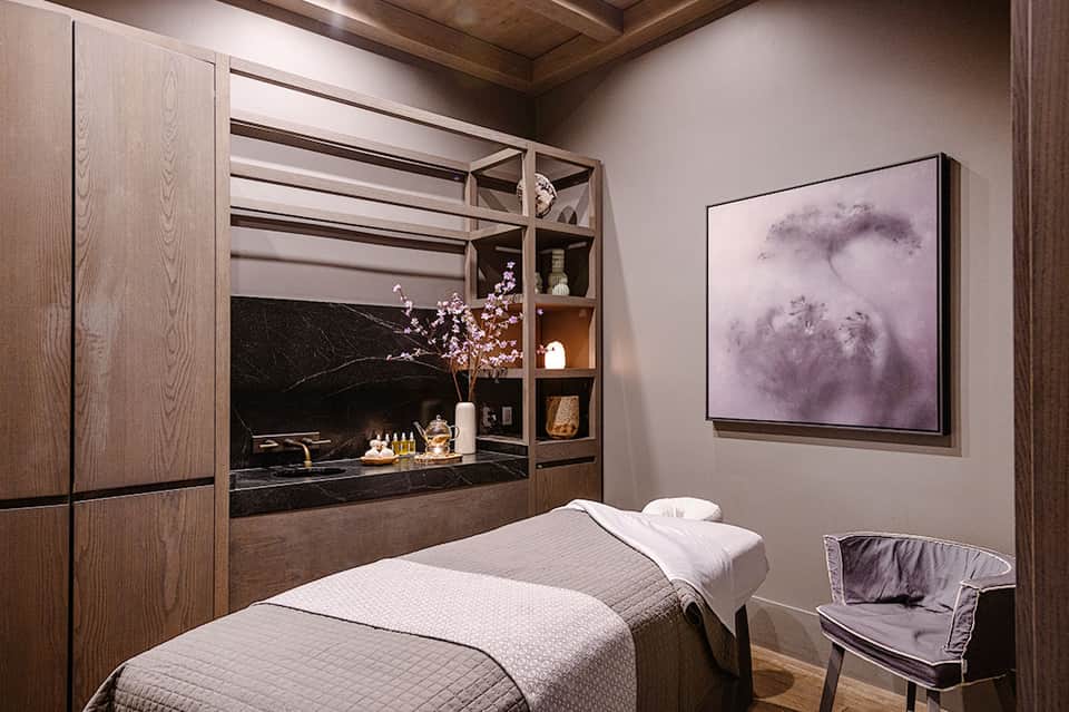 Spa treatment room with massage bed, dark wood cabinetry, and modern black marble vanity