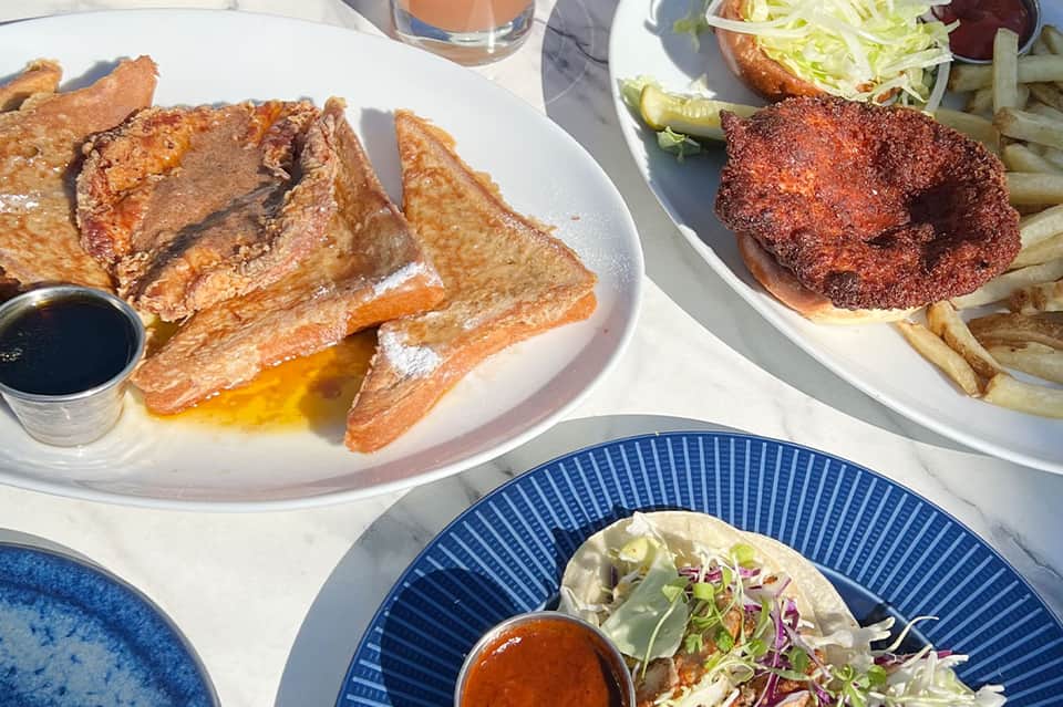 Overhead view of poolside lunch featuring French toast, spiced burger with fries, and appetizers