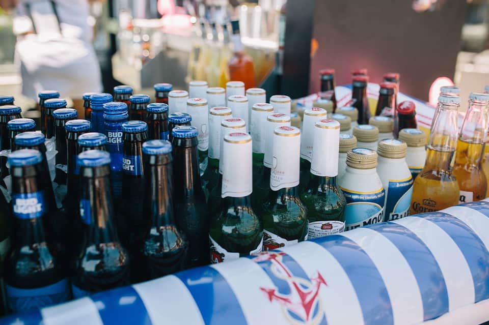 Beer and beverage bottles arranged on striped table at outdoor event