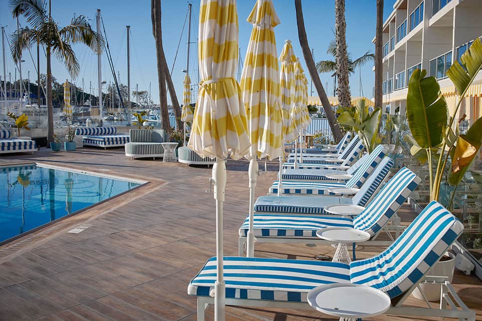 Waterfront pool with yellow and white striped umbrellas, sailboats, and marina views in background
