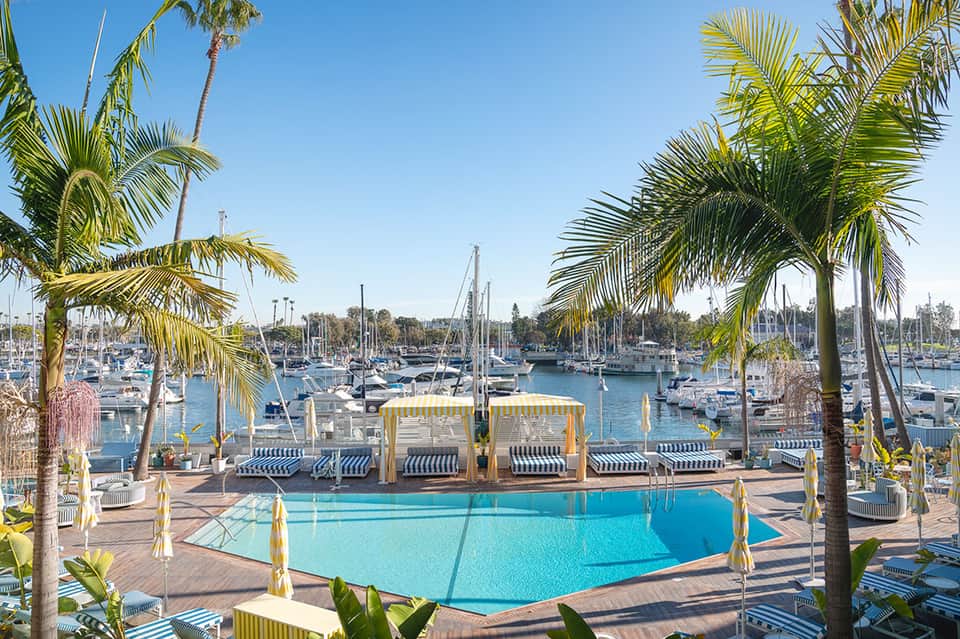 Marina-view resort pool with yellow umbrellas, striped cabanas, and sailboats in background