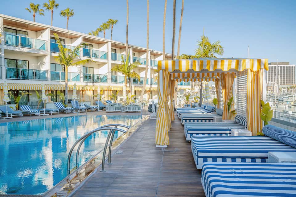 Modern resort pool deck with yellow striped cabanas, lounge chairs, and high-rise building