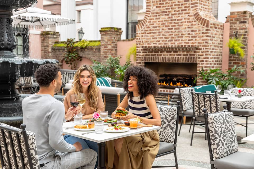 Three guests dining on patio with brick fireplace, fountain, and decorative patterned seating
