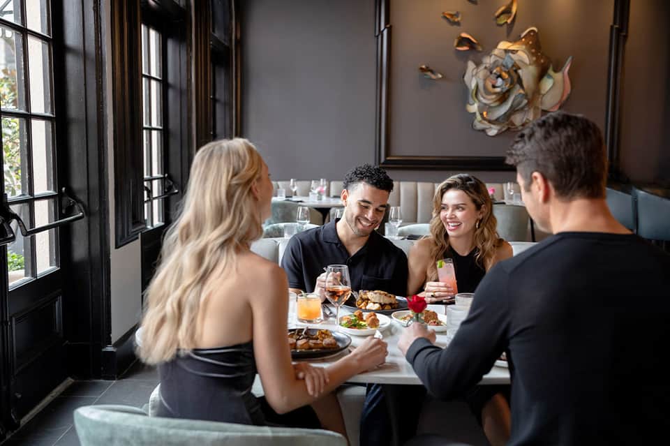 Four guests dining together at elegant restaurant with dark walls and artwork