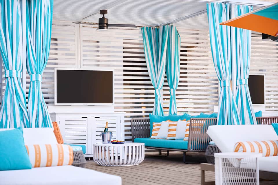 Cabana lounge with striped curtains, turquoise cushions, and modern outdoor entertainment setup