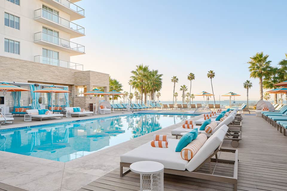 Resort pool with turquoise water, white loungers with blue and orange accents, and palm trees