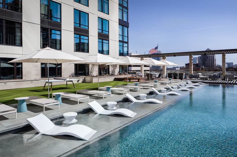 Modern hotel poolside with white lounge chairs, umbrellas, and waterfront views
