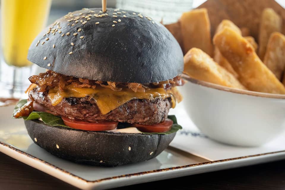 Upscale burger with black sesame seed bun, melted cheese, tomato, and served with golden fries