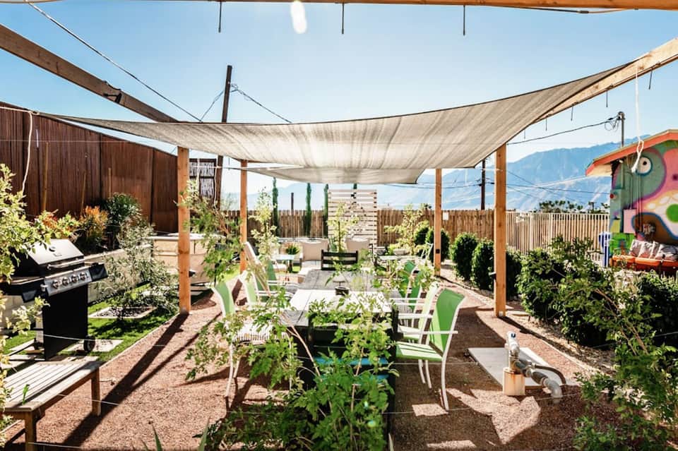 Outdoor patio with shade sails, lounge chairs, garden plants, grill, and mountain views